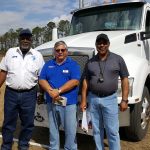 Three smiling men standing in front of semi truck